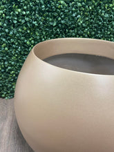 Charger l'image dans la galerie, An artificial tree with lush green round leaves in a matte gold round planter, placed against a white wall next to a glass-paneled door in a minimalistic room.