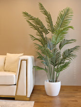 Charger l'image dans la galerie, Artificial palm plant in a modern white ceramic pot, placed beside a luxurious white sofa with gold accents, creating a chic and contemporary living room decor