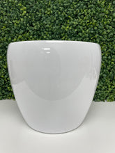 Charger l'image dans la galerie, A simple and sleek white ceramic planter with a glossy finish, positioned in front of a green artificial foliage wall. The planter has a rounded, tapered shape with a smooth surface.