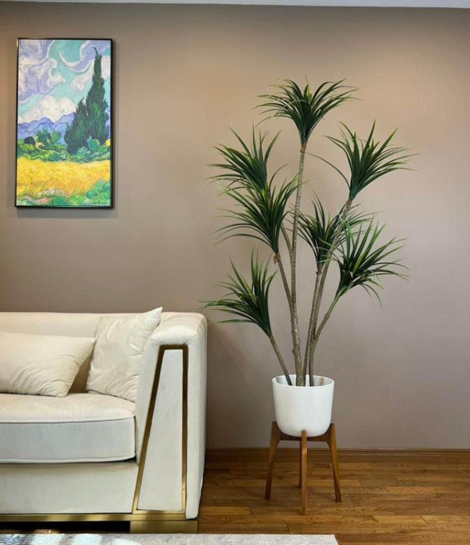 An artificial plant in a white pot besides a white sofa in the living room.