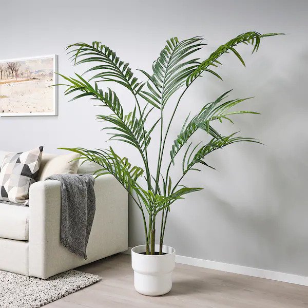 An indoor artificial plant in the white pot with white sofa besides the plant.