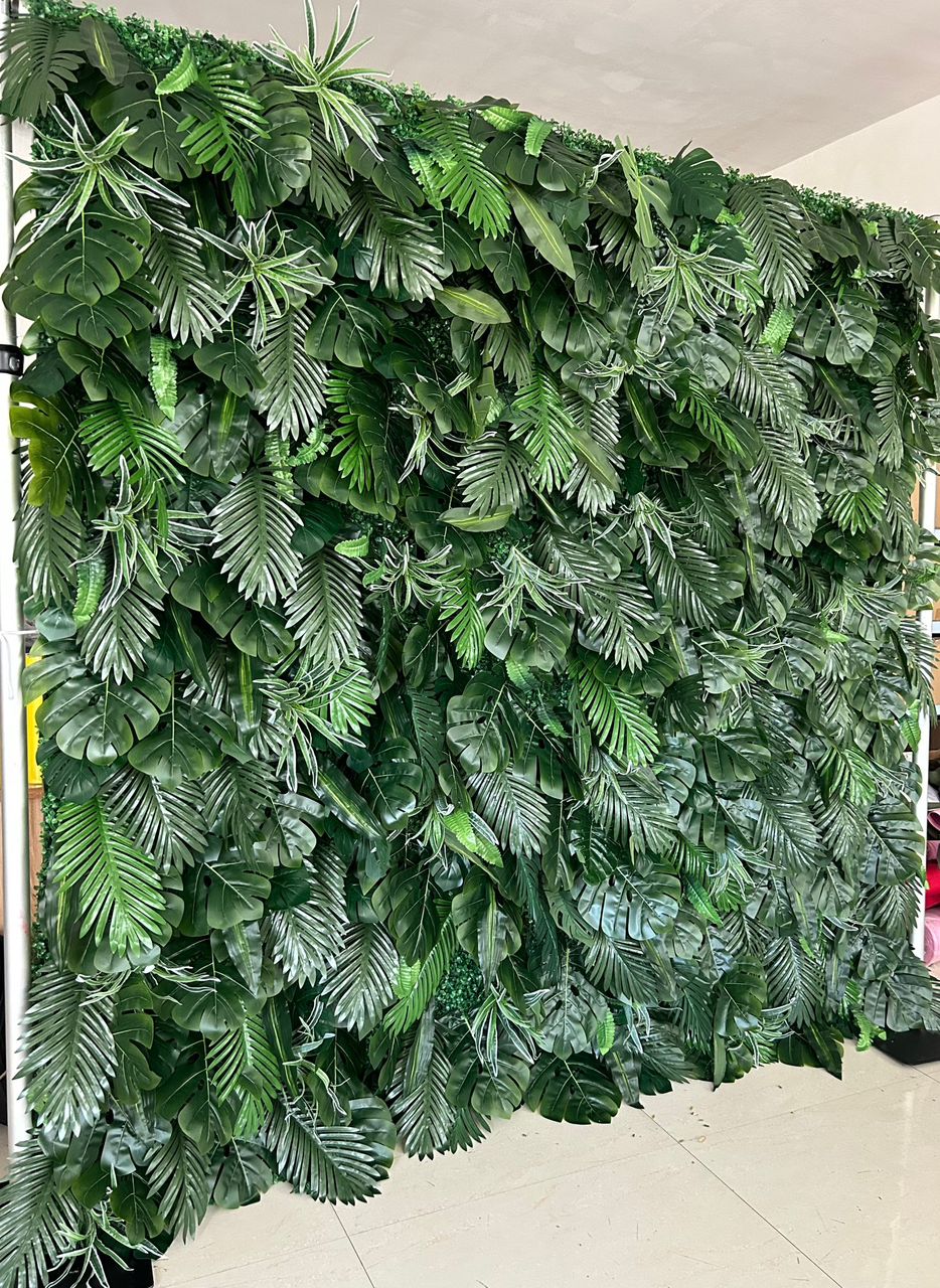 Artificial tropical green leaf backdrop featuring a variety of realistic foliage. Perfect for event decoration, photo booths, and indoor or outdoor settings. How durable is this artificial greenery wall for extended outdoor use? Can the individual leaves or sections be rearranged for custom designs?
