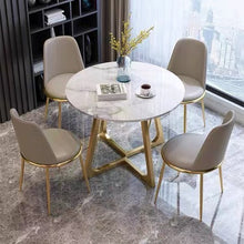 Load image into Gallery viewer, Elegant Round Dining Table with Glossy Sintered Stone Top and Gold Metal Legs, Surrounded by Four Grey Upholstered Chairs in Modern Apartment Setting with Marble Flooring
