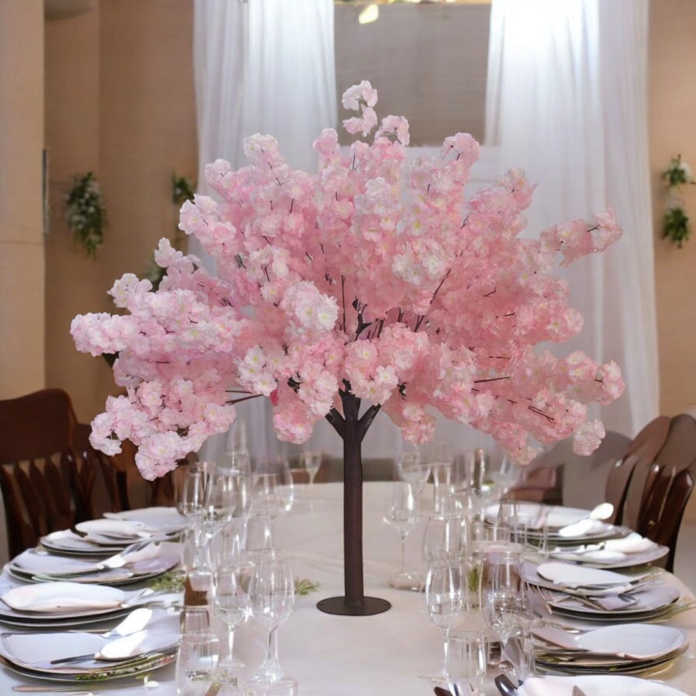 Decorative pink cherry blossom tree centerpiece on a table with place settings.