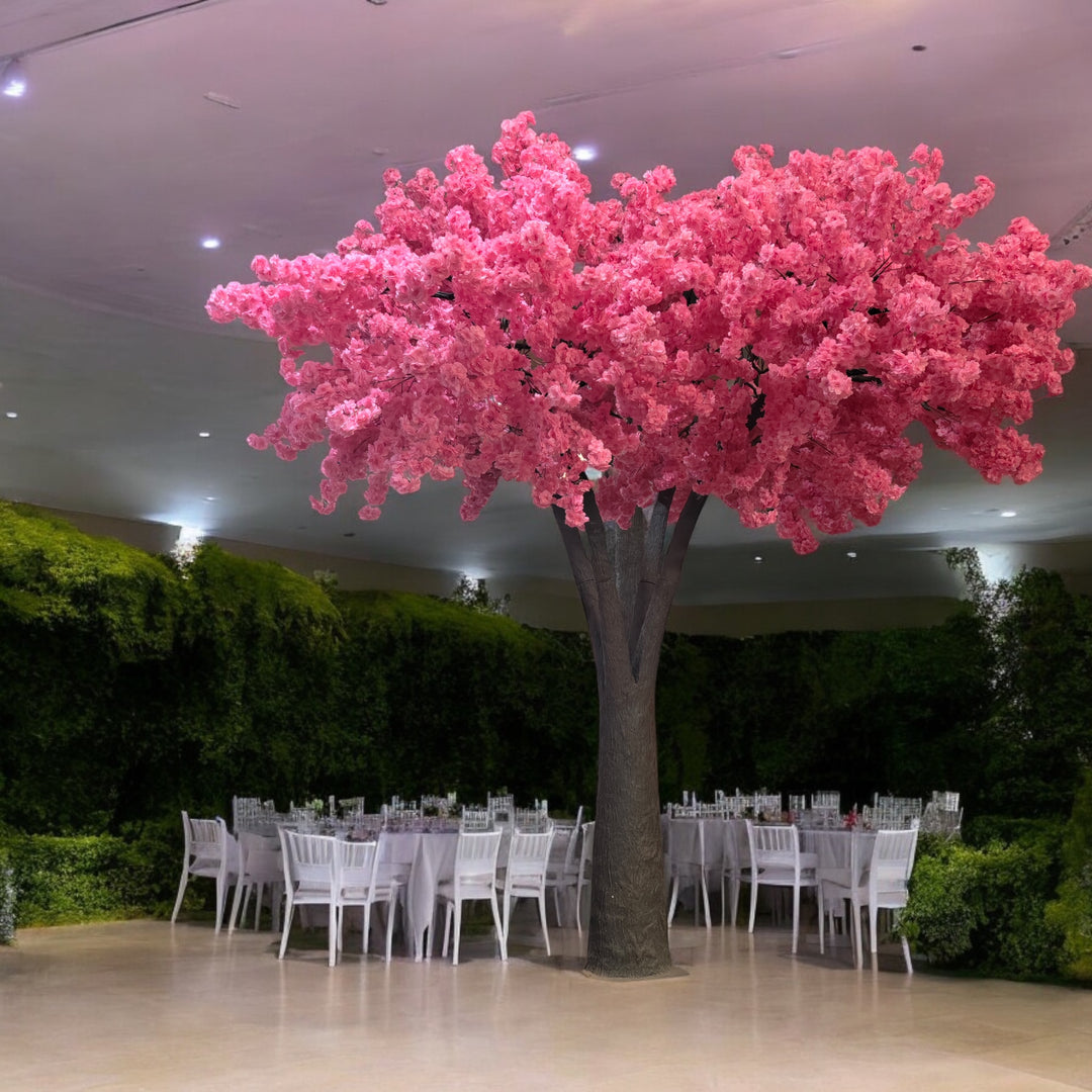 Artificial tree with pink blossoms, creating a romantic atmosphere in a wedding venue adorned with white chairs, floral centerpieces, and soft lighting. Are these rental trees available in varying heights to suit different event spaces?