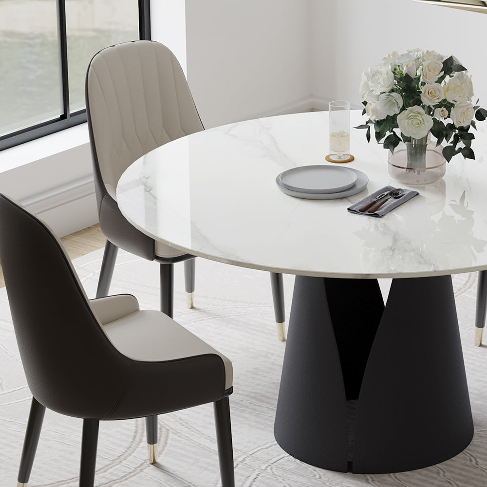 Modern dining area featuring a round marble table with a unique black base, accompanied by two stylish chairs with beige and dark gray upholstery. The table is set with elegant tableware and a floral centerpiece, creating a sophisticated and inviting atmosphere