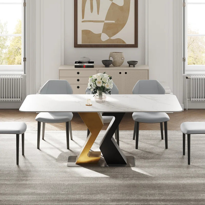 Contemporary white rectangular dining table with striking black and gold angular geometric base, complemented by sleek gray dining chairs
