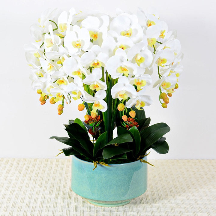 A large arrangement of artificial white orchids with lush green leaves in a modern white planter. Frequently asked question: What are the best planters to use for artificial plants to enhance their aesthetic appeal?