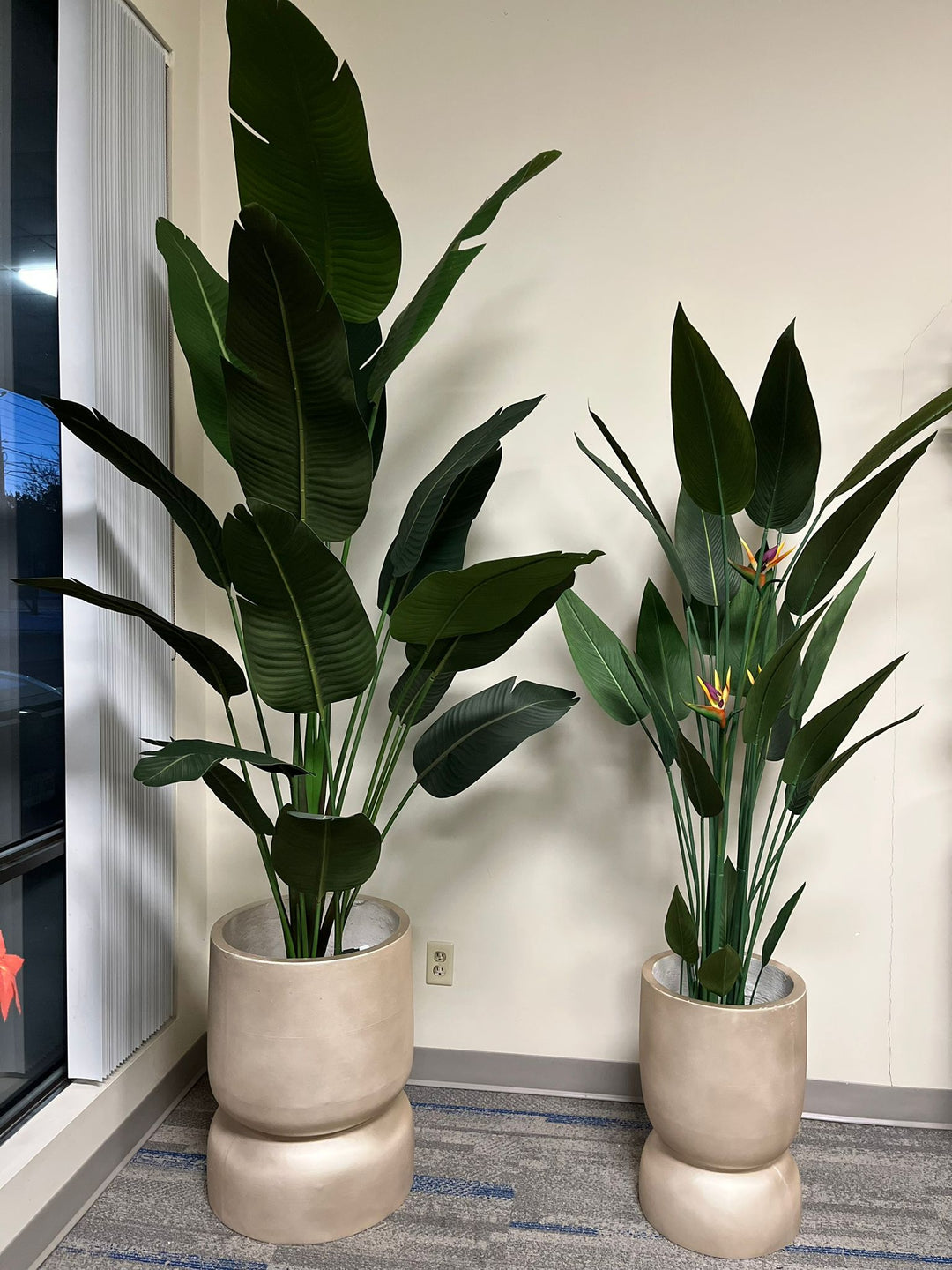 Pair of tall golden stackable planters with a smooth matte finish, each holding artificial plants with large green leaves, placed indoors near a window with natural light. Are these planters made from lightweight materials for easy mobility?"