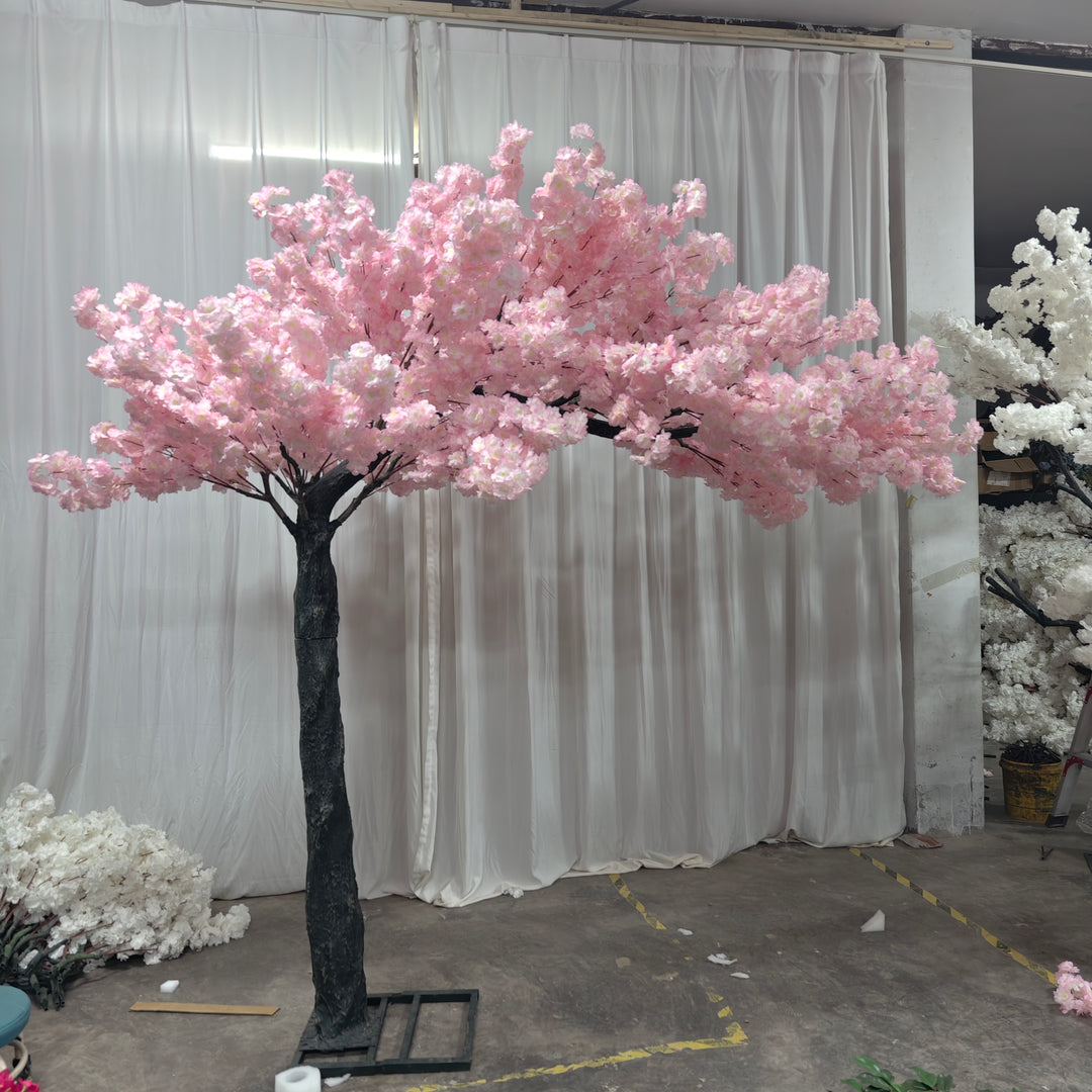 Stunning artificial light pink cherry blossom tree displayed in a professional setup with white curtains in the background, ideal for wedding and event decor. How can this cherry blossom tree enhance your event's aesthetic?