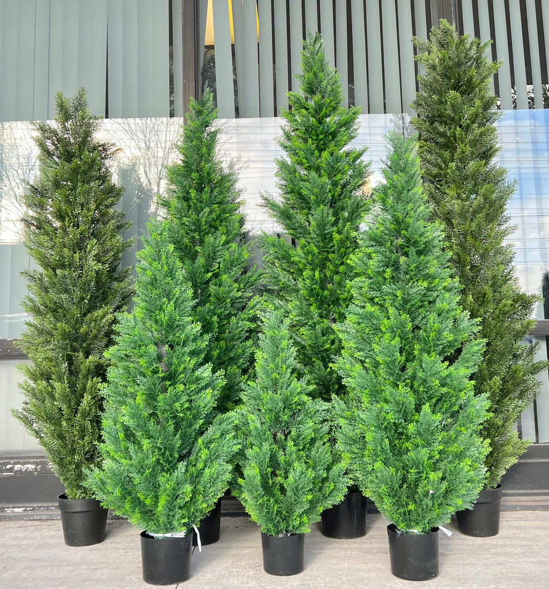 Collection of artificial evergreen trees in varying sizes, all potted in black containers, arranged outdoors against a window, ideal for creating a lush, natural ambiance in any setting.