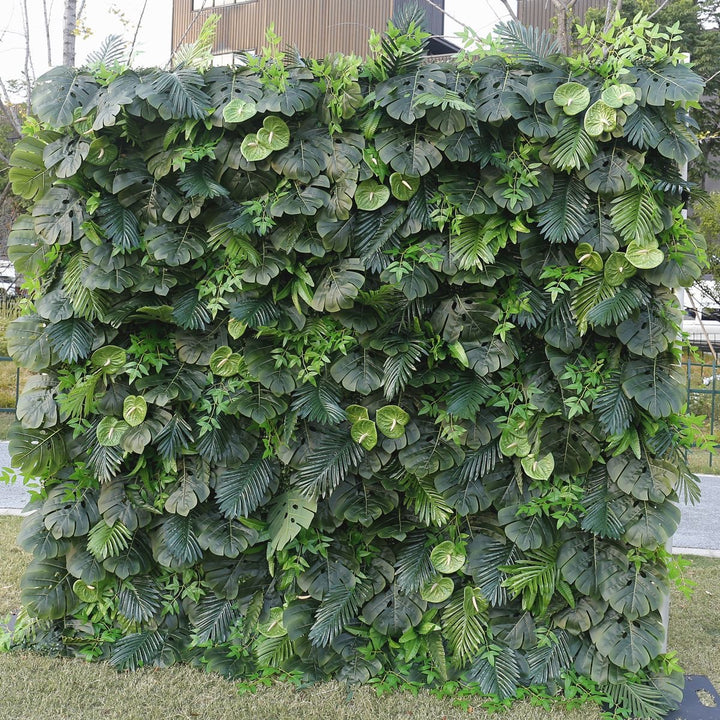 Artificial greenery wall featuring a variety of green tropical leaves, designed for event backgrounds, commercial spaces, and indoor plant decor. Can this backdrop add a natural ambiance to any space? Is it durable enough for high-traffic areas?