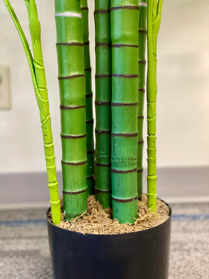 Close-up of artificial palm tree trunks in a black pot, showcasing realistic green bamboo-style stems.