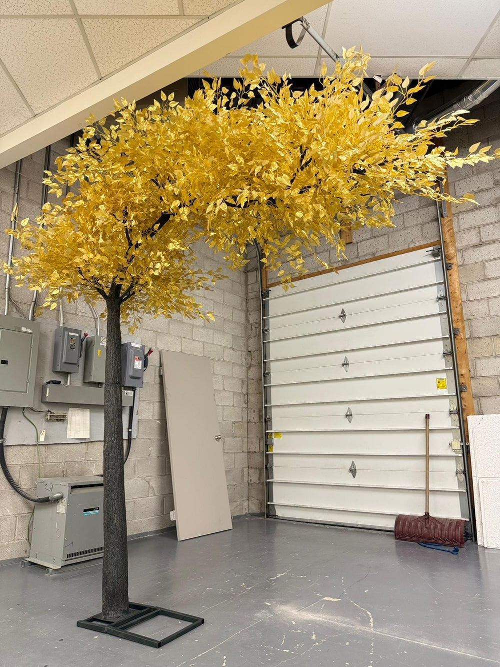 Artificial yellow tree in a warehouse setting with a garage door in the background.