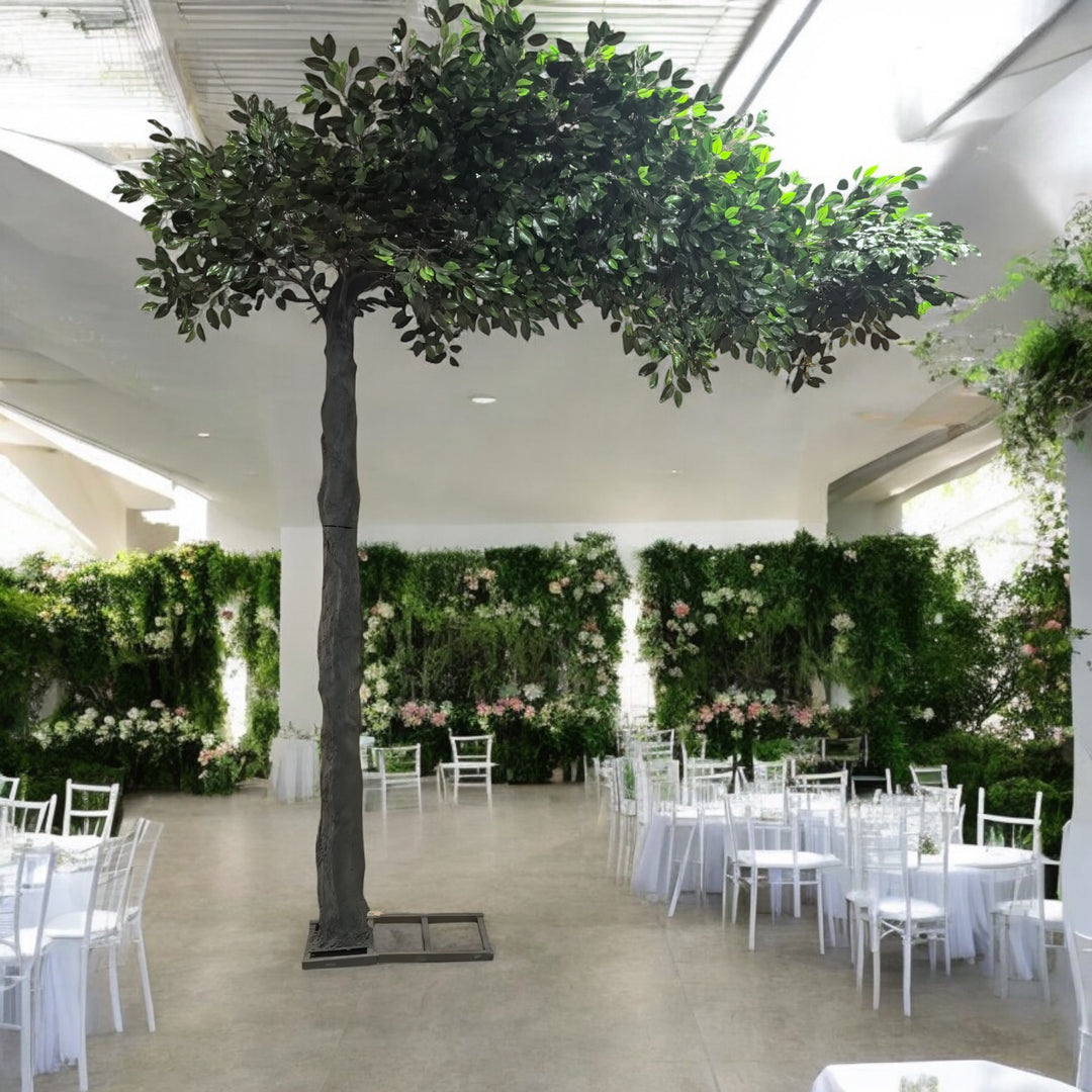 Artificial green arch ficus tree with dense foliage, elegantly set in a wedding venue adorned with white round tables and a lush floral backdrop. 