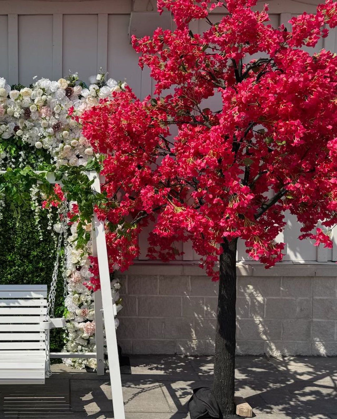 Artificial hot pink bougainvillea flowering tree with a white floral arch against a light-colored wall.