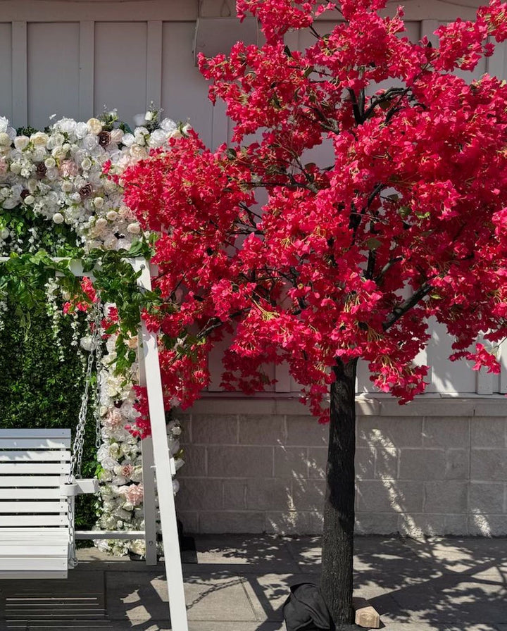 Artificial hot pink bougainvillea flowering tree with a white floral arch against a light-colored wall.