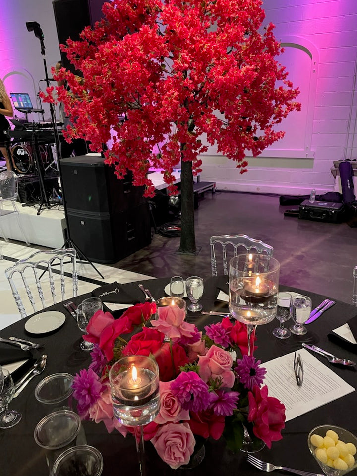Decorative table setting with hot pink bougainvillea flowers, candles, and glasses in a formal event setting.