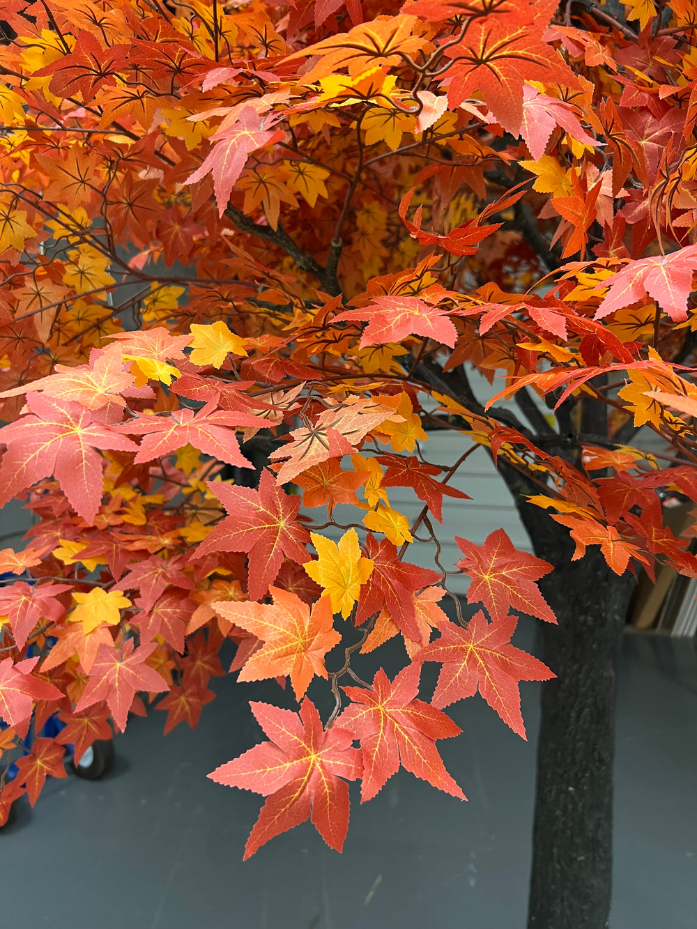 Artificial maple leaf branch with red, orange, and yellow leaves on a dark background.