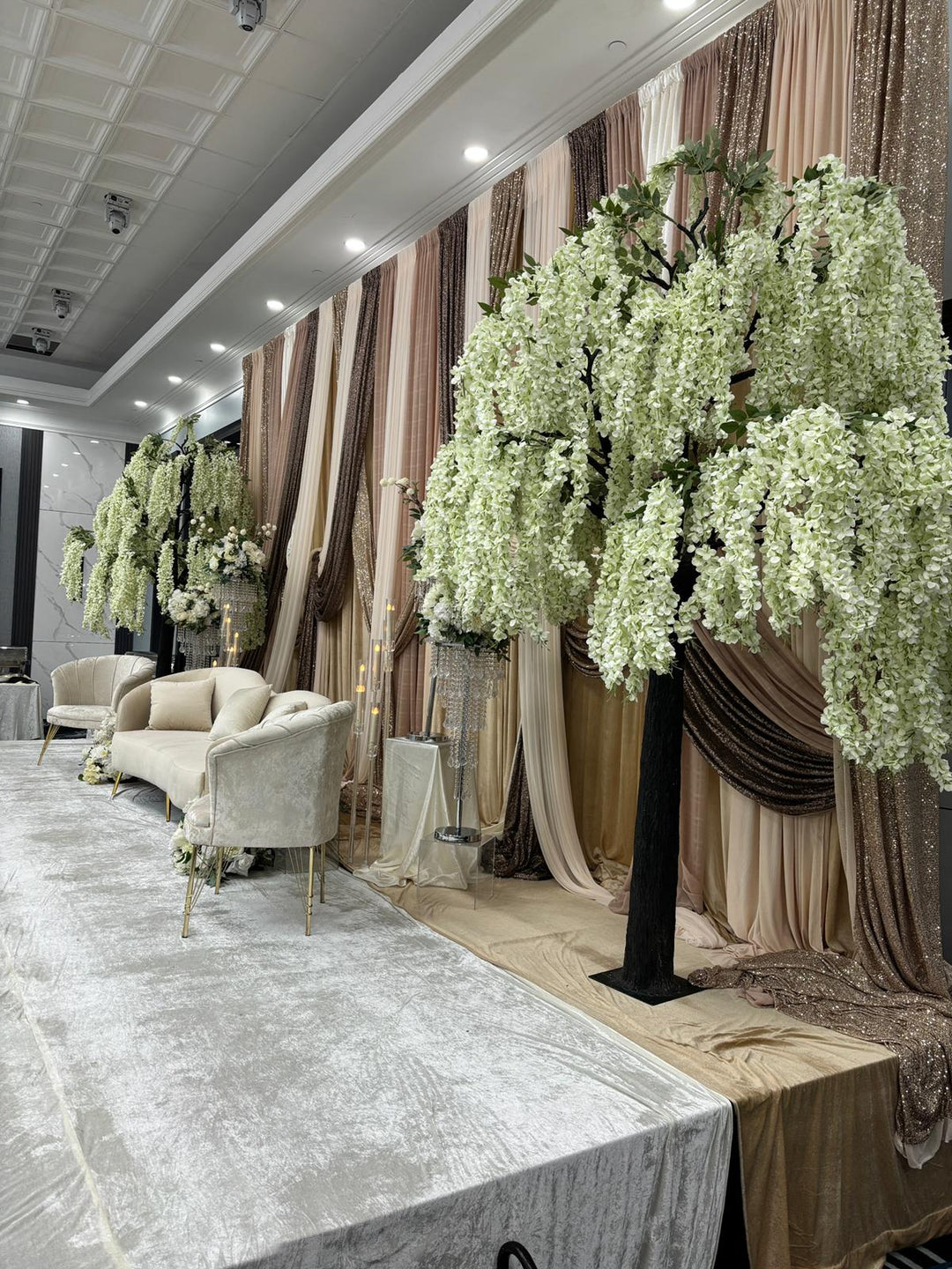 Decorative setup with white wisteria floral arrangements and draped curtains in a room.