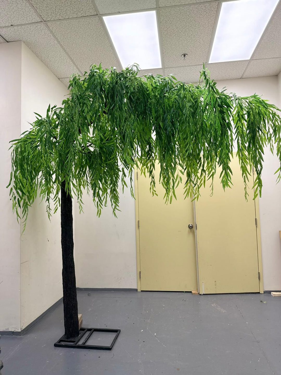 Elegant artificial arch willow tree placed in the corner of a room with cascading green leaves.