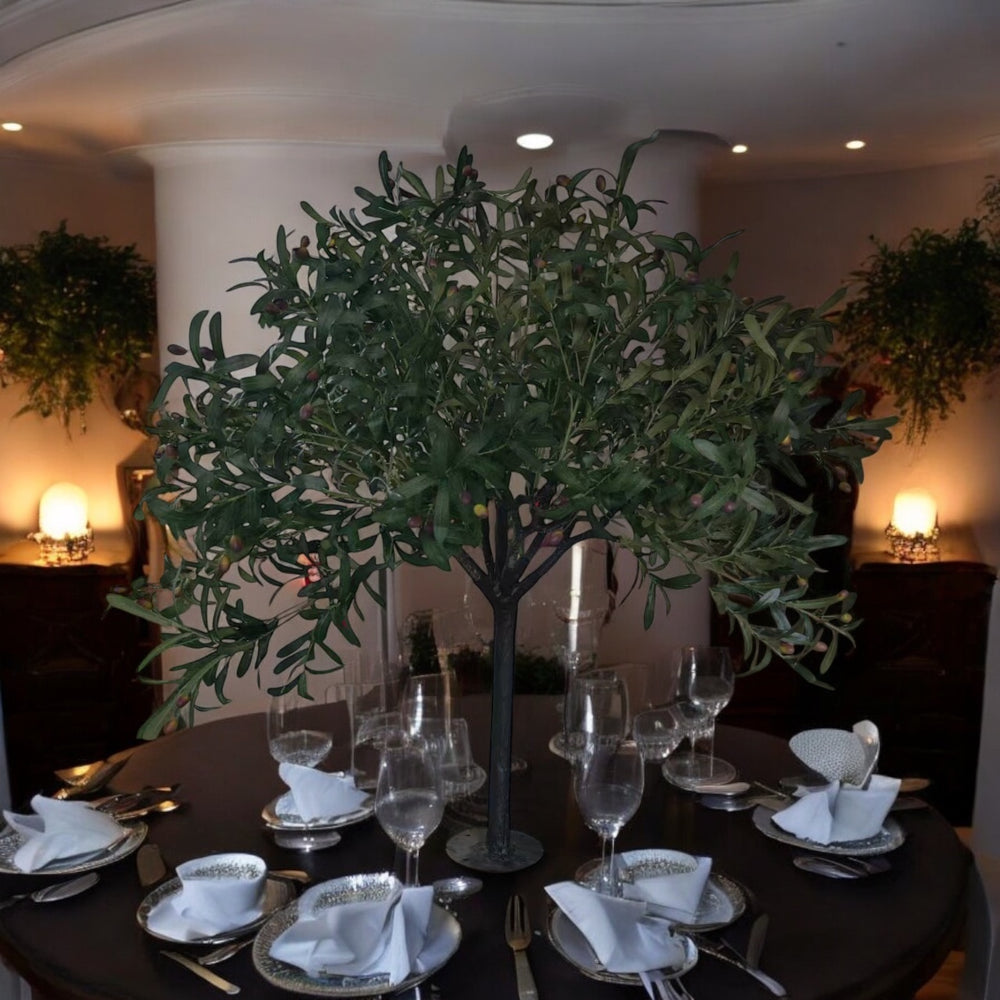 Dining table set with plates, glasses, and cutlery, featuring a large green plant centerpiece.
