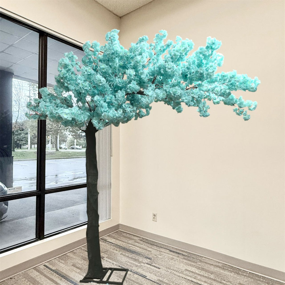 An artificial arch cherry blossom tree with soft blue blossoms and a dark textured trunk, standing indoors near a window with a gray patterned floor.