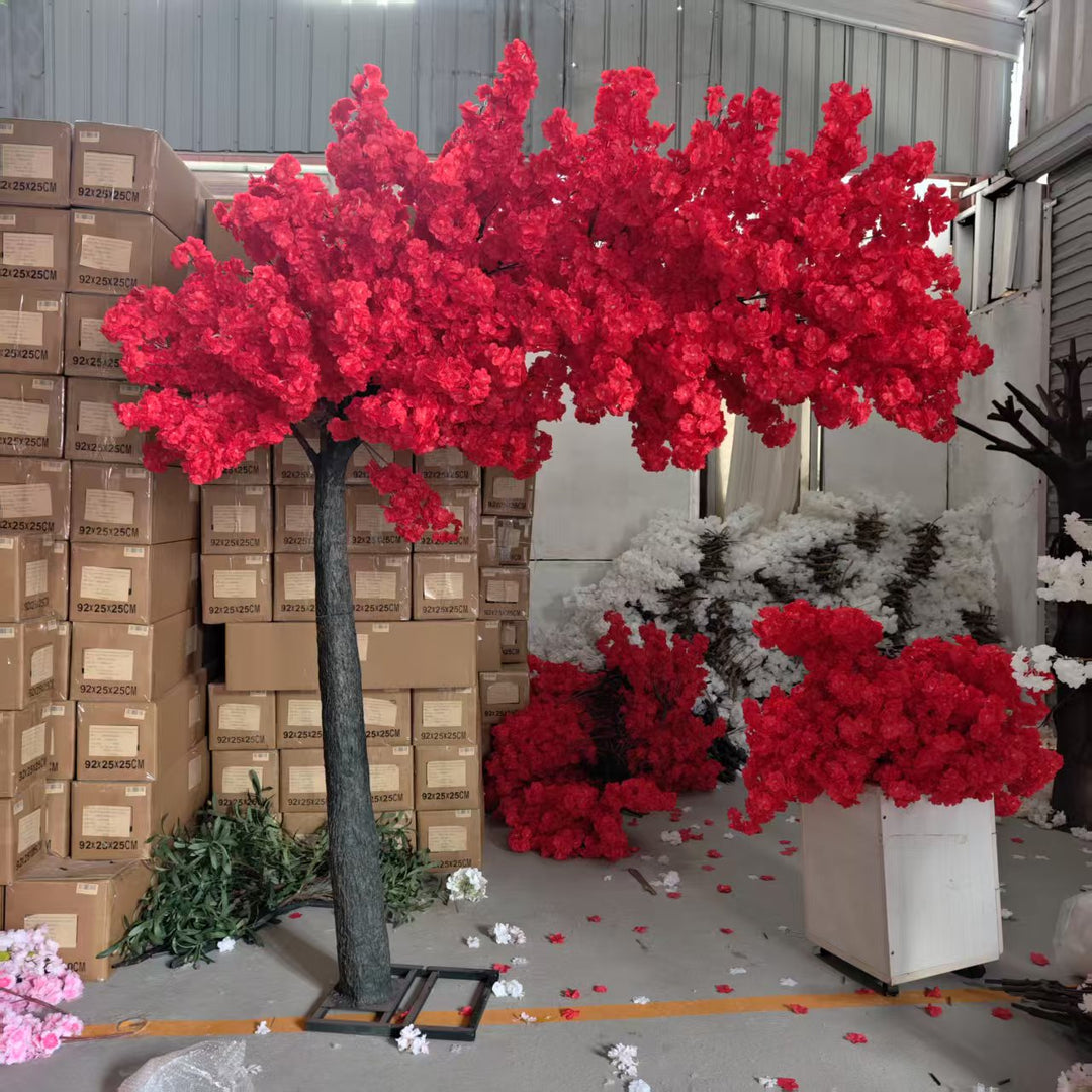 Red artificial cherry blossom arch trees in a warehouse setting with cardboard boxes.