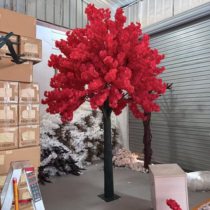 Red artificial cherry blossom tree in a warehouse setting with boxes and materials around