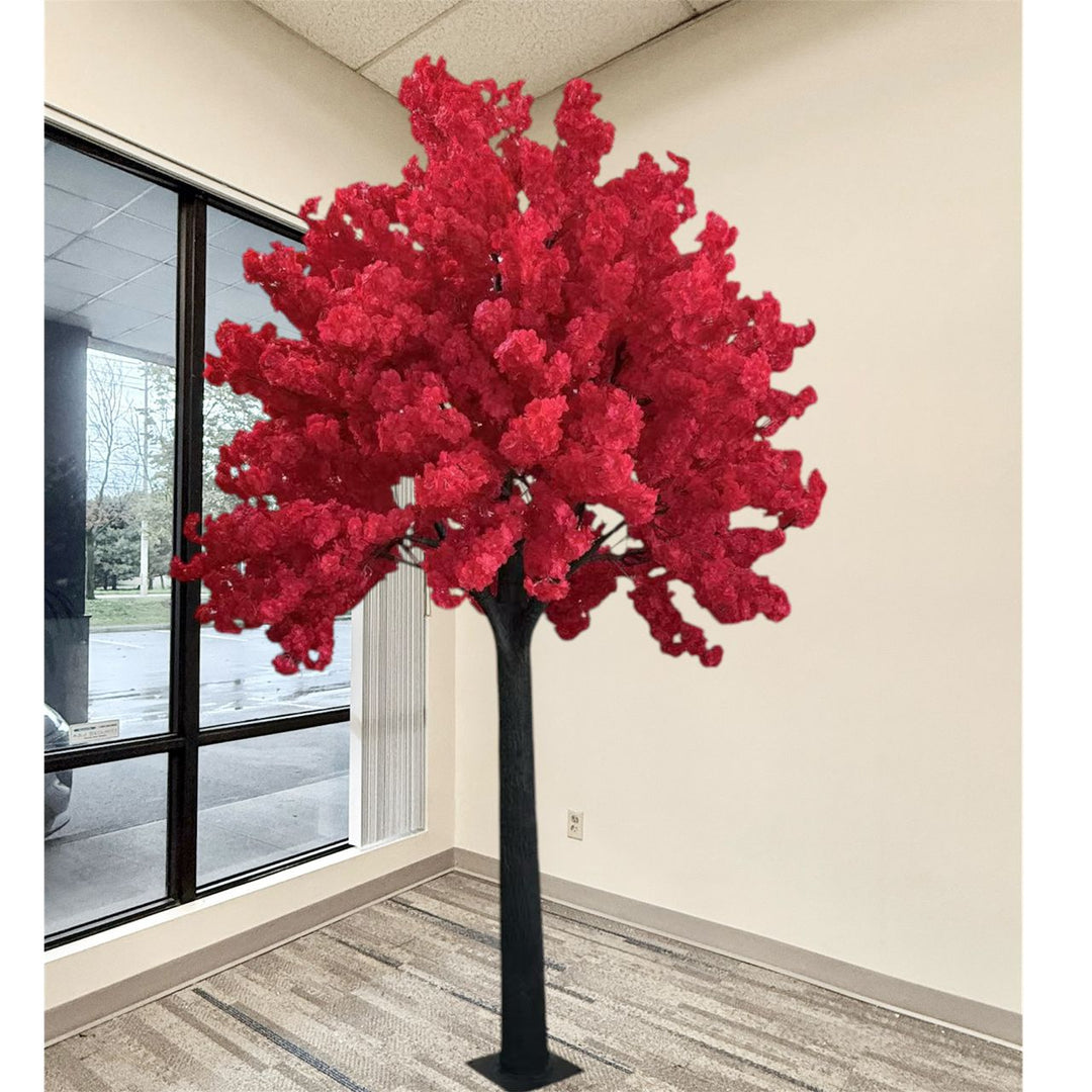 A large artificial cherry blossom tree with vibrant red flowers and a black trunk, standing in a modern office lobby next to a window.