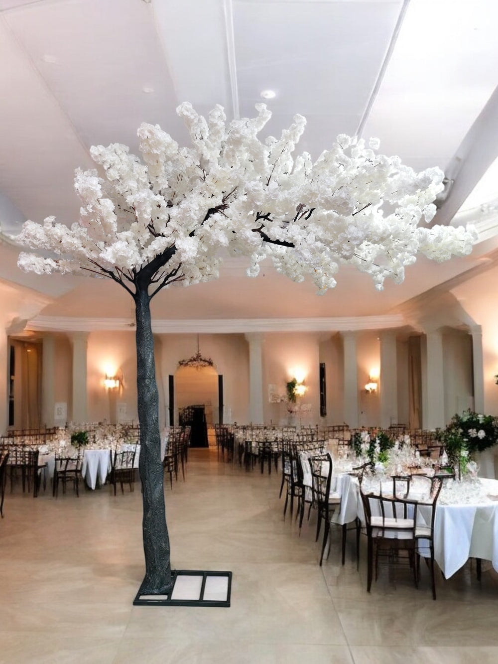 A luxurious indoor wedding venue decorated with a stunning artificial white cherry blossom tree centerpiece.