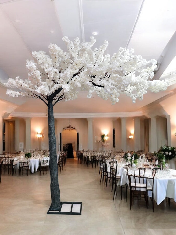 A luxurious indoor wedding venue decorated with a stunning artificial white cherry blossom tree centerpiece.