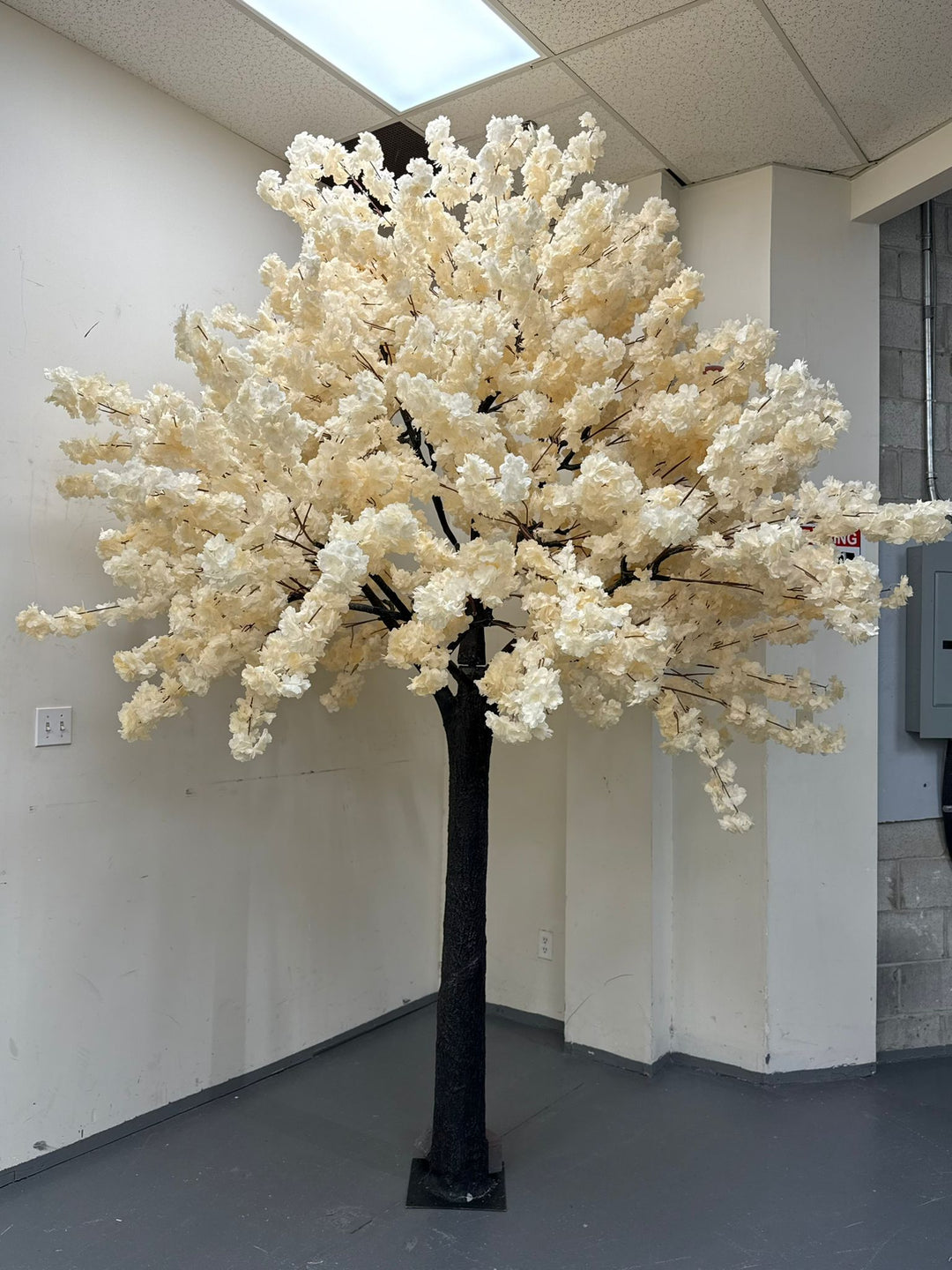 Decorative faux cream white tree in an indoor setting with a plain wall and floor.