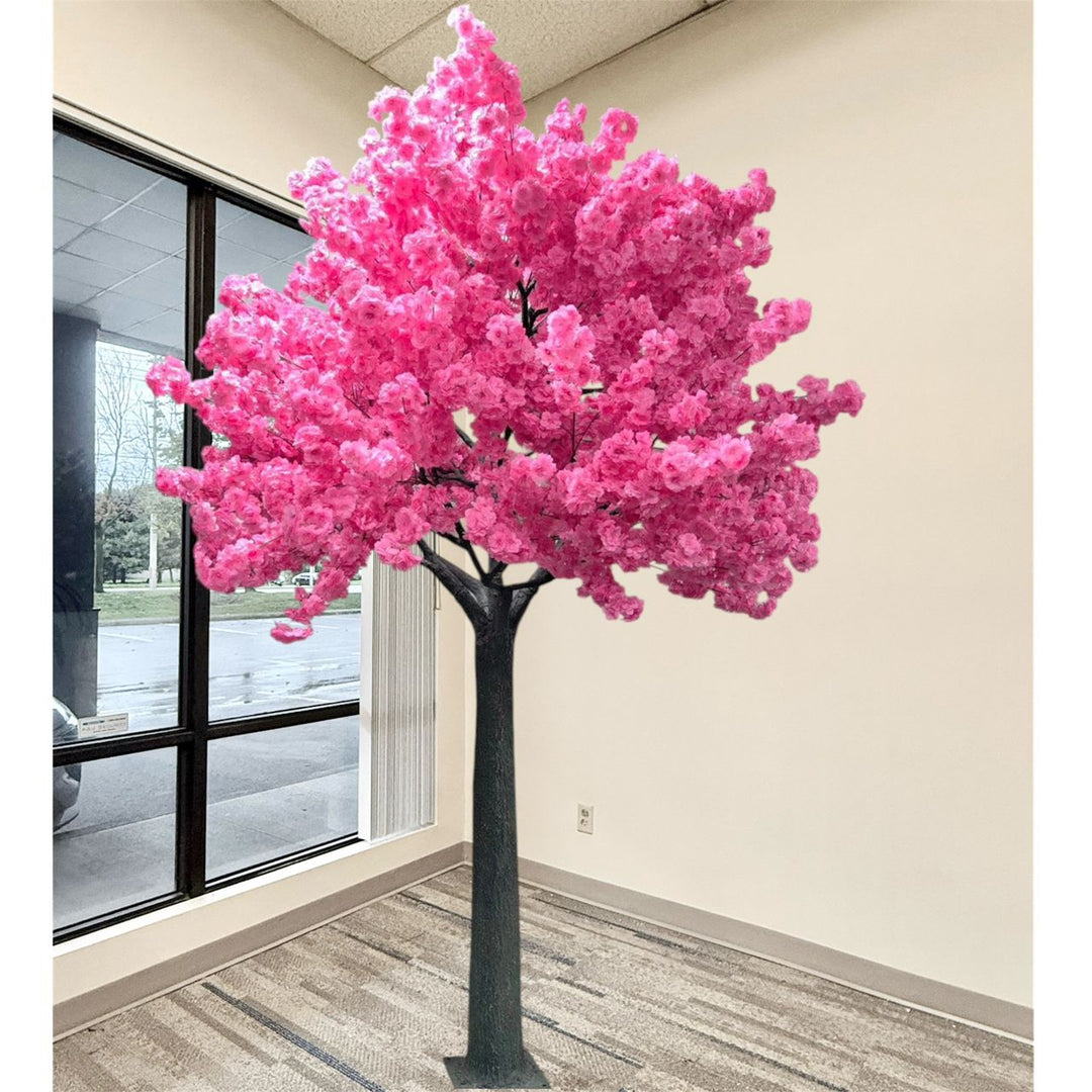 A large artificial dark pink cherry blossom tree with vibrant pink blossoms and a dark textured trunk, set indoors next to a window with beige walls and striped carpet.