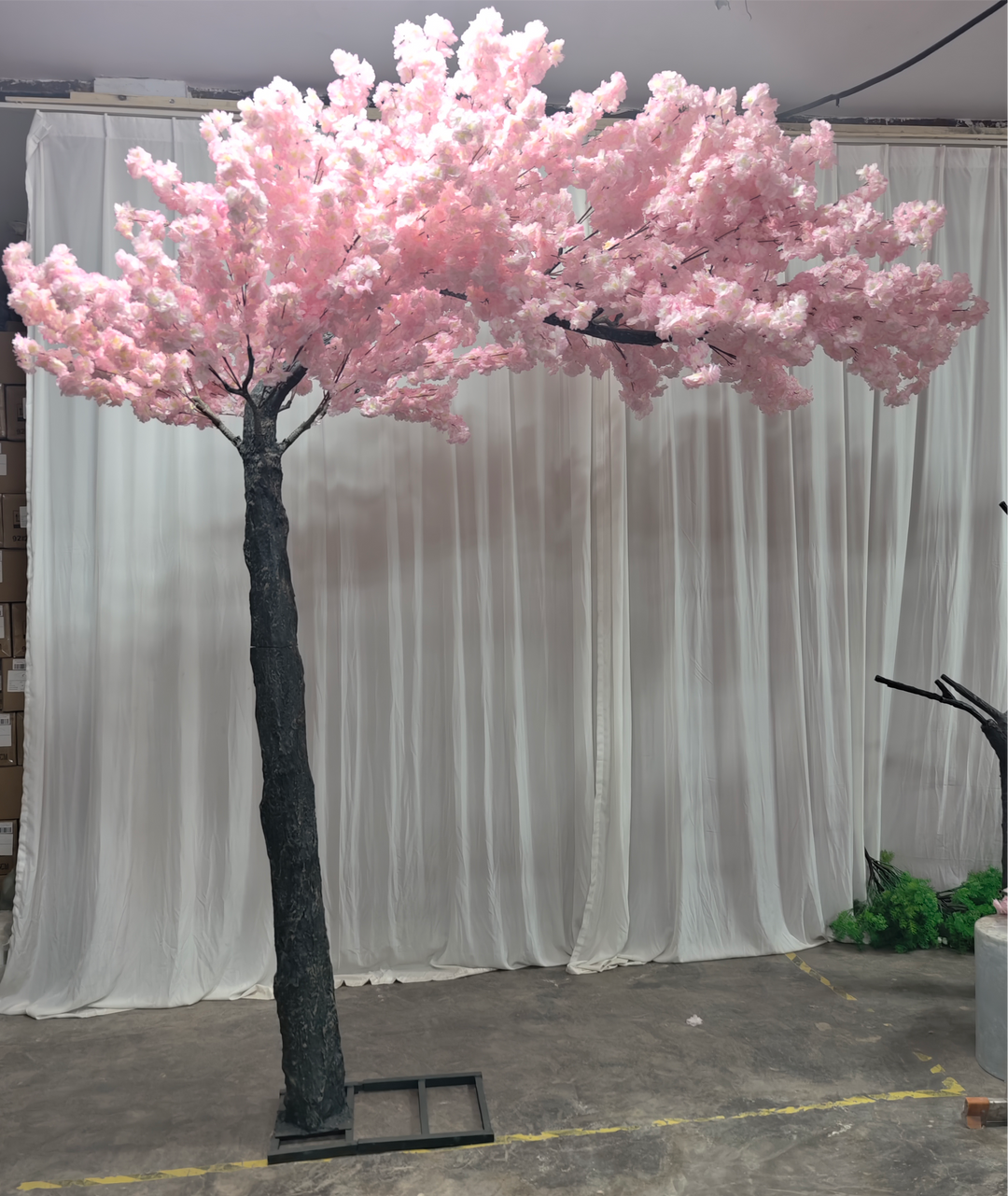 Artificial cherry blossom arch with realistic pink flowers in front of a white drape backdrop.
