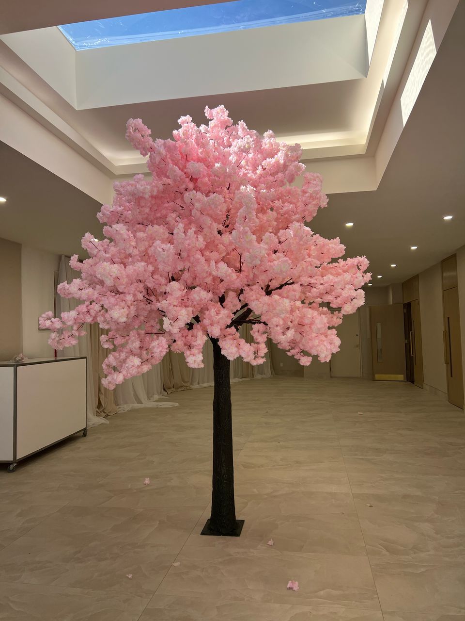 An artificial 10ft cherry blossom tree with light pink flowers, placed indoors at a venue as a decorative element.