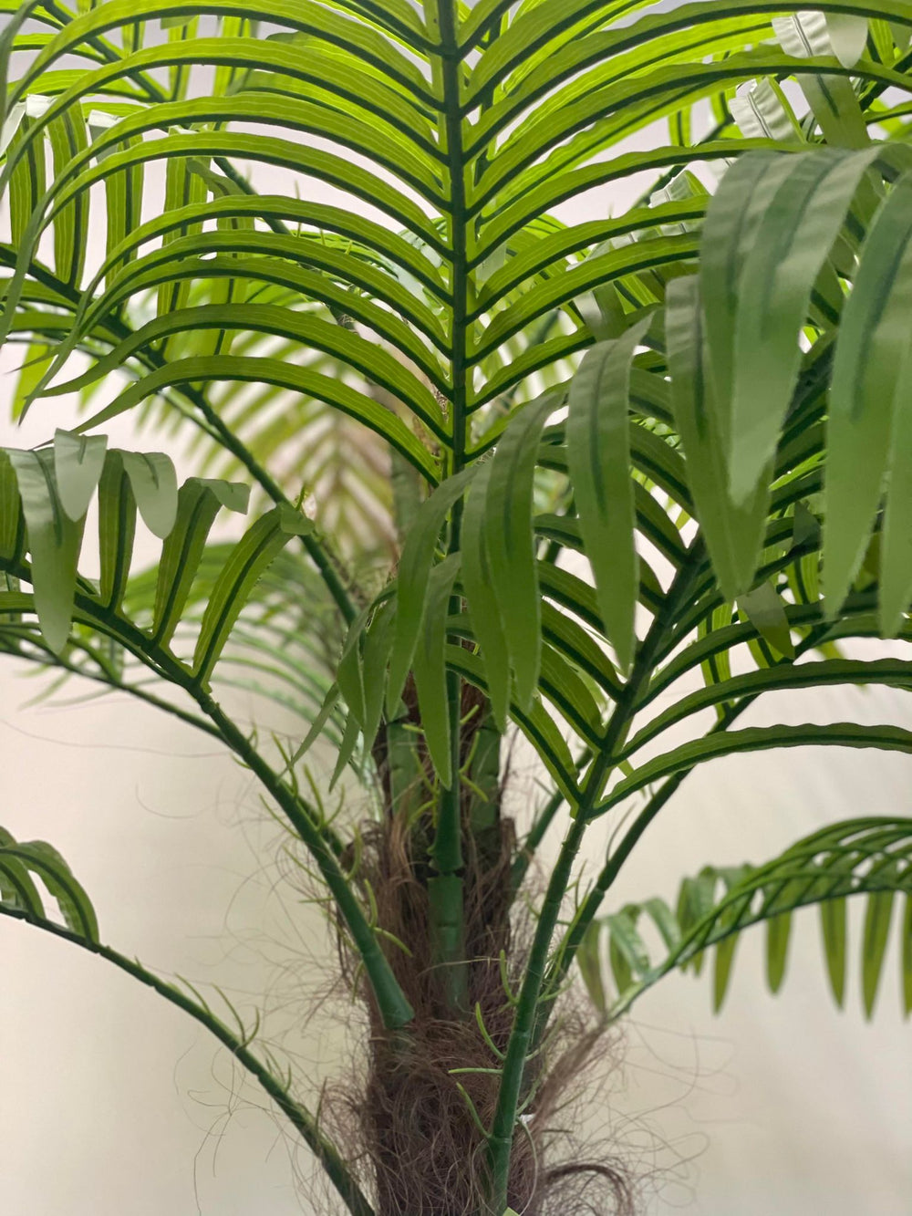 Close-up view of an artificial palm tree, showcasing realistic green fronds and detailed textured trunk with natural-looking fibers.