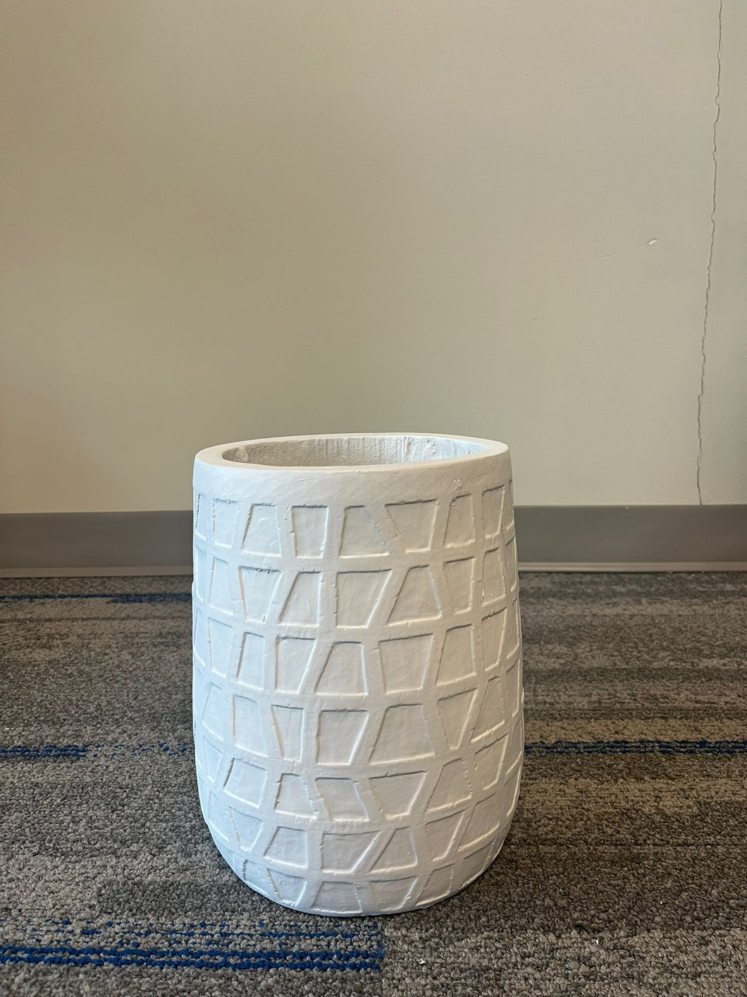 White planter with a geometric textured design, displayed empty indoors on a carpeted floor against a neutral background. What are the height and diameter dimensions of this planter?