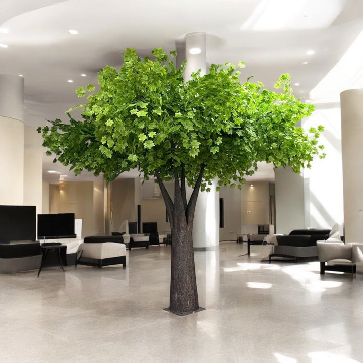 Large artificial green maple indoor tree in a modern office setting with white walls and gray flooring.