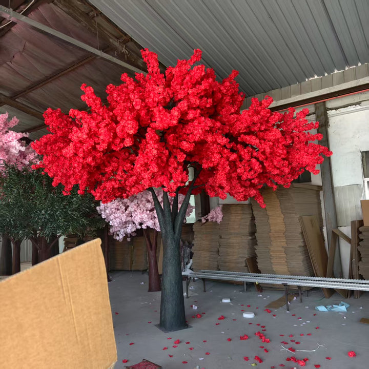 Red artificial cheryy blossom tree in a warehouse setting with cardboard boxes and other materials.