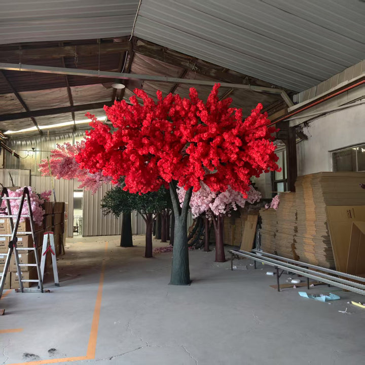 Red artificial cherry blossom tree in a warehouse setting with cardboard boxes and equipment.