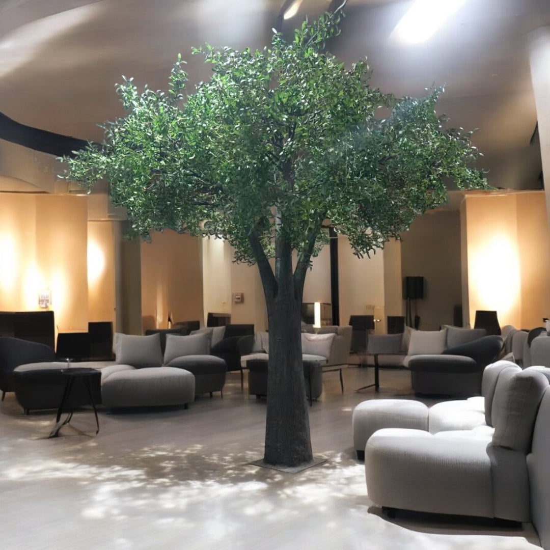 Modern interior with gray sofas, a large artificial olive tree, and wall-mounted speakers.