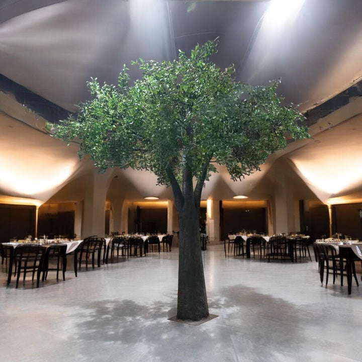 Large artificial olive tree in a room with tables and chairs, likely a dining or event space.