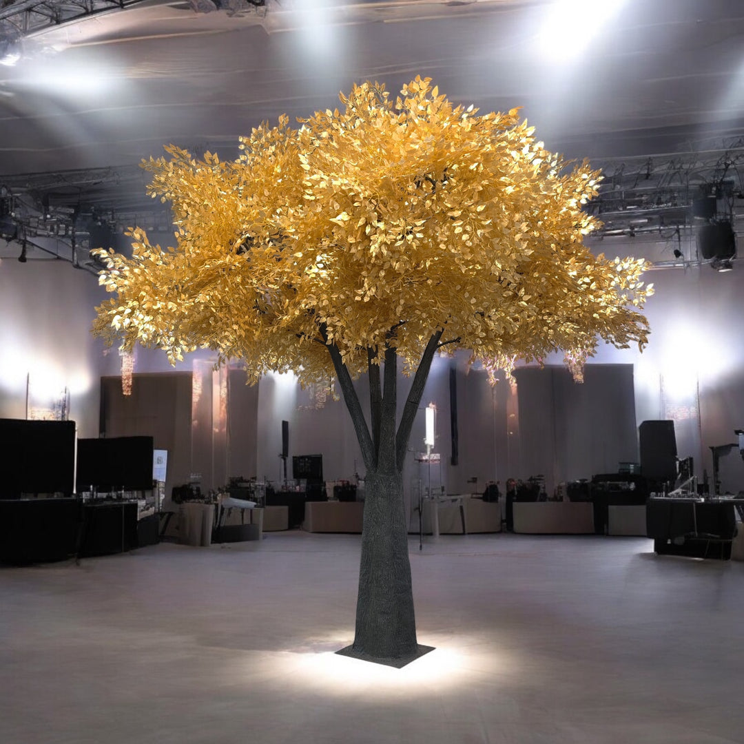 Large artificial ficus tree with gold leaves in a room with tables and chairs.