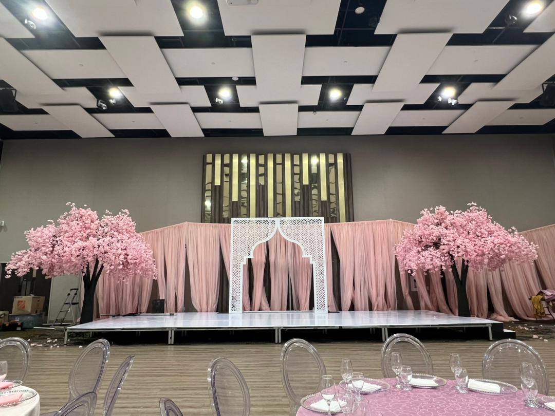 Decorated event space with pink weeping cherry blossoms floral arrangements and a stage.