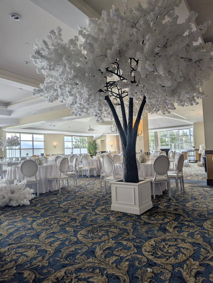 Decorative white cherry blossom  tree in a room with tables and chairs, likely a banquet hall.