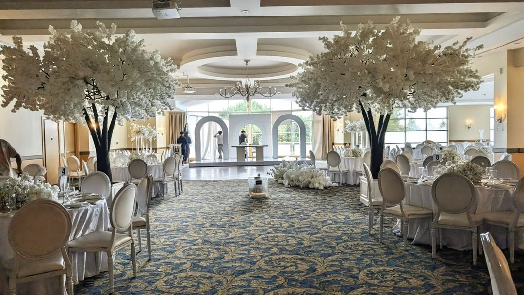 Grand banquet hall with tables, chairs, and white cherry blossom floral decorations.