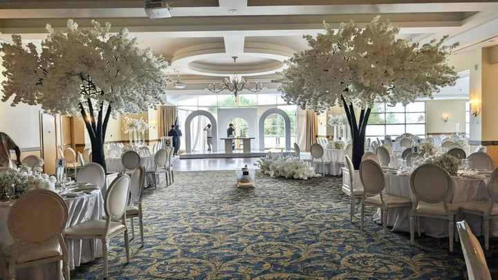Grand banquet hall with tables, chairs, and white cherry blossom floral decorations.