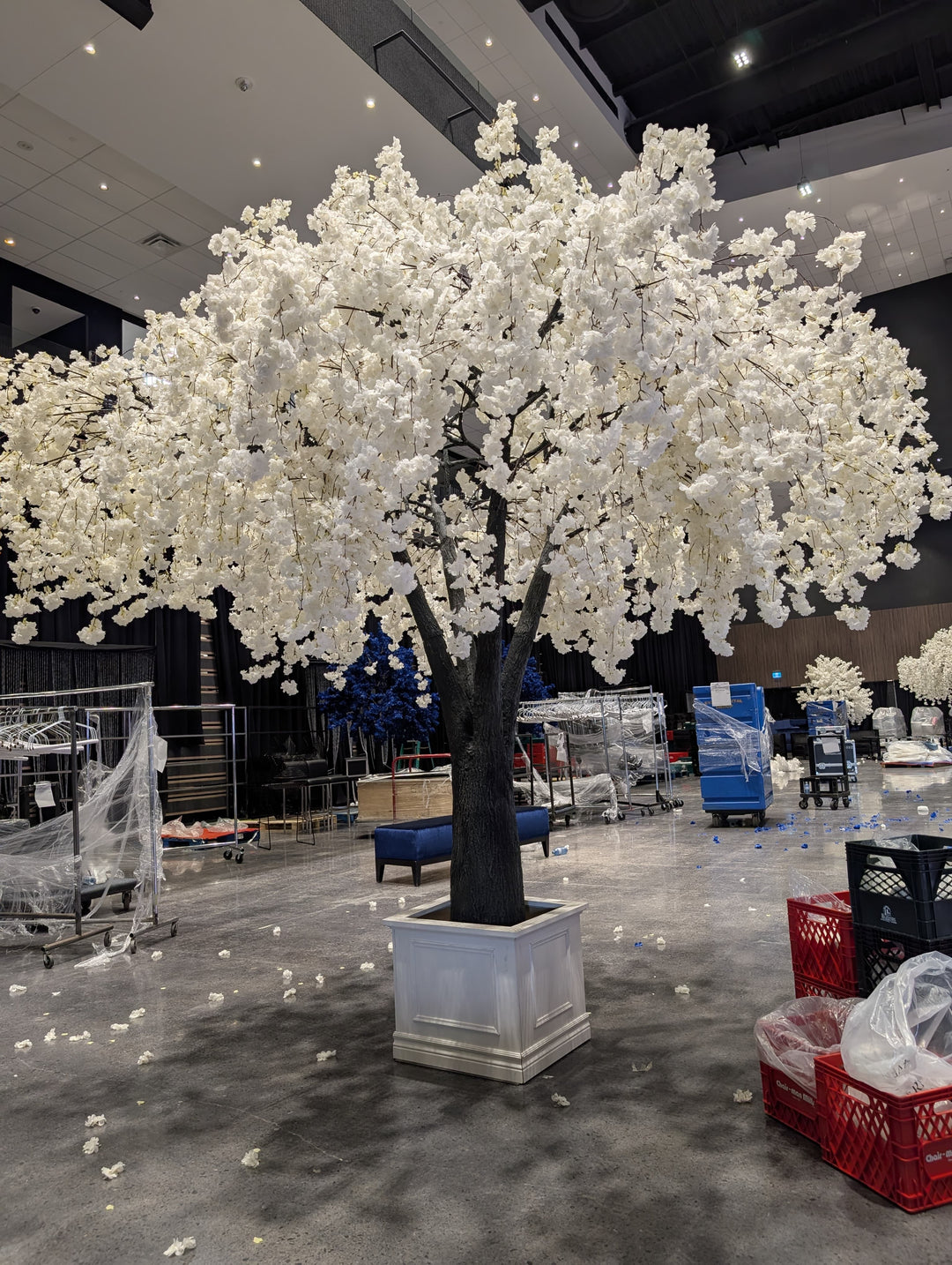 Large artificial white weeping cherry blossom flowering tree in a store setting with various items and people in the background.