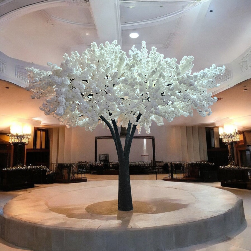 Grand artificial tree with cascading white blossoms, beautifully displayed as a centerpiece on a raised platform in a luxurious wedding venue. Can these rental trees be customized to fit specific event designs and themes?